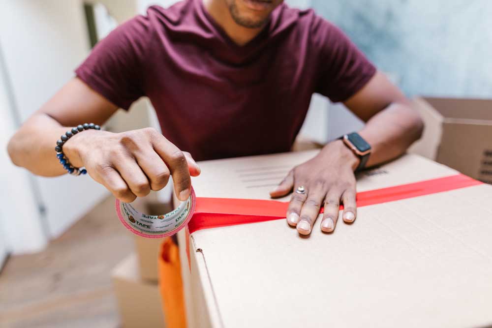 Man sealing moving box with red packing tape