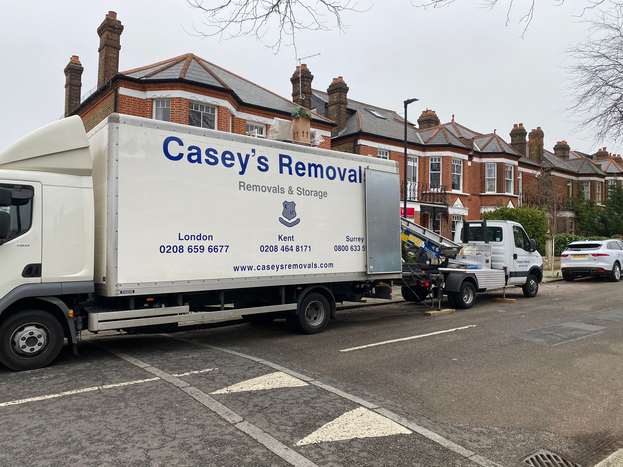 House Removal Truck with Casey's Removals printed on side parked outside a house with a hoist moving items from top window.