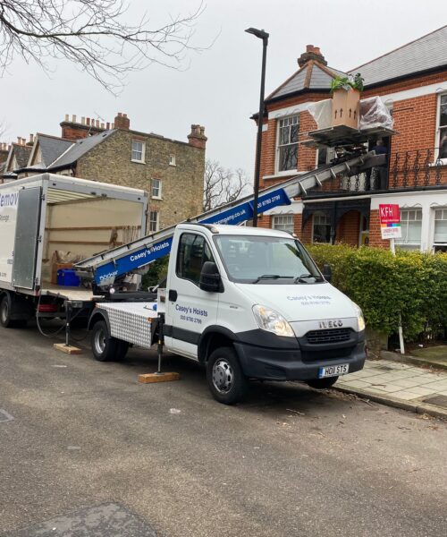 House Removal Truck with Casey's Removals printed on side parked outside a house with a hoist moving items from top window.