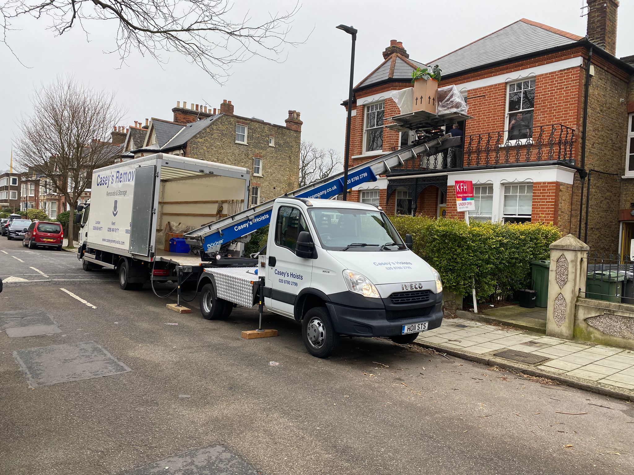 House Removal Truck with Casey's Removals printed on side parked outside a house with a hoist moving items from top window.