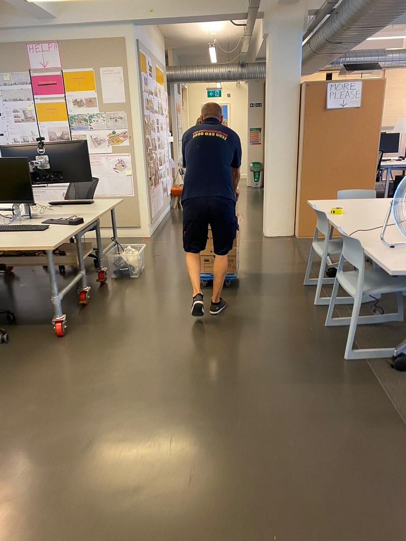 Man pushing furniture inside office wearing a dark tshirt with casey's removals printed on back