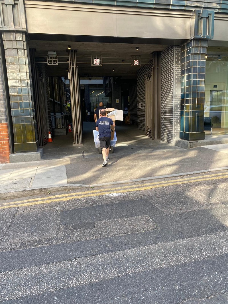 Men carrying office furniture outside of office building wearing a dark tshirt with casey's removals printed on back