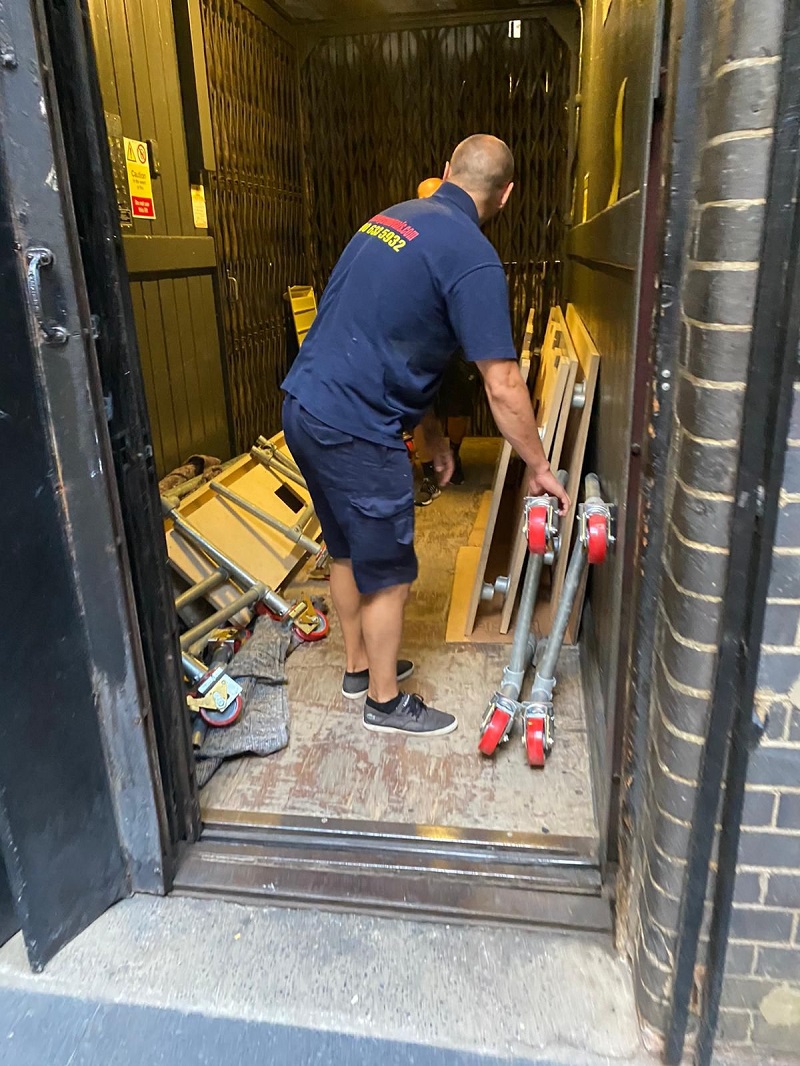 Man wearing a dark tshirt with casey's removals printed on back picking up office furniture